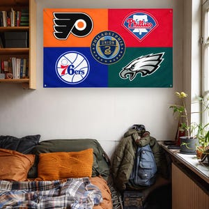 May include: A rectangular wall flag featuring four colored quadrants with Philadelphia sports team logos. The top left is orange with the Flyers logo, top right is red with the Phillies logo, bottom left is blue with the 76ers logo, and bottom right is green with the Eagles logo. A circular Philadelphia Union crest is centered.