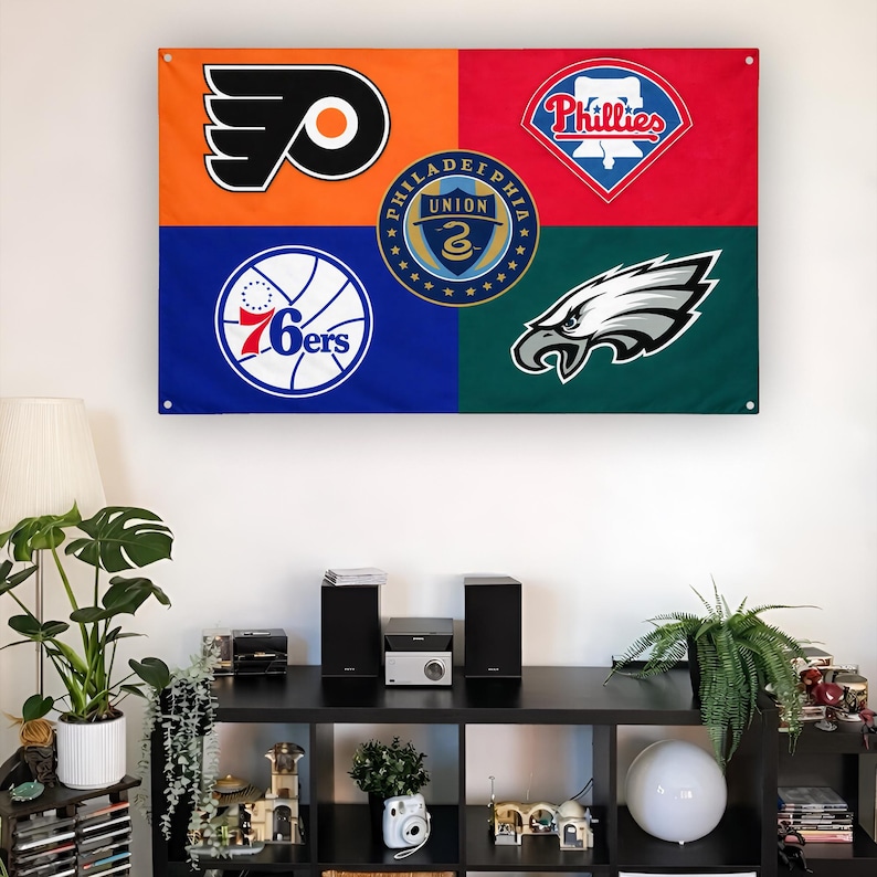 May include: A rectangular wall flag featuring four quadrants in orange, red, blue, and dark green. It displays the Philadelphia Flyers, Phillies, 76ers, and Eagles logos, with the Philadelphia Union crest centered in the middle of the flag.