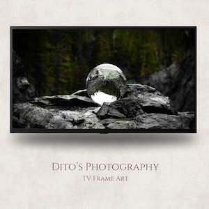 May include: A black TV frame art print showing a clear glass sphere on a dark, textured rock. The background features a blurred green forest. The text "Dito's Photography TV Frame Art" is at the bottom.