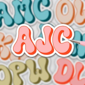 Könnte beinhalten: Ein Aufkleber mit den Buchstaben "AJC" in einem Retro-Schriftstil, hellrosa mit einer leuchtend orangefarbenen Umrandung. Der Aufkleber befindet sich auf einem weißen Hintergrund, mit anderen Aufklebern im Hintergrund.