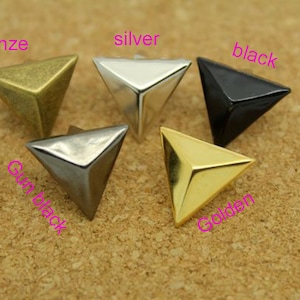 May include: Five triangular pyramid-shaped metal studs in different colours: bronze, silver, black, gunmetal, and gold.