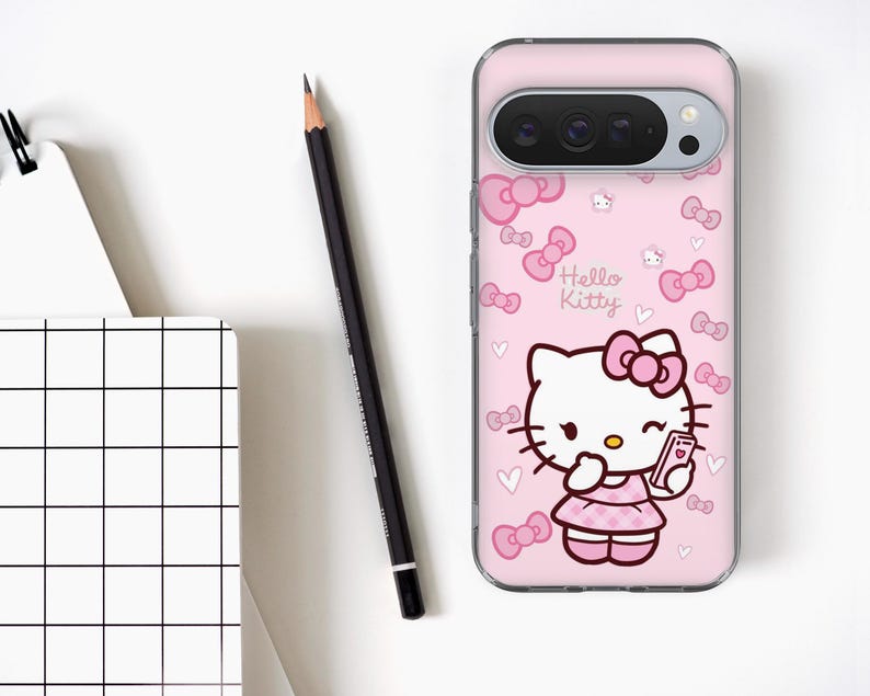Puede incluir: Una funda de tel&eacute;fono rosa con el personaje de Hello Kitty sosteniendo un tel&eacute;fono. La funda tiene un patr&oacute;n repetido de lazos y corazones rosas. Un l&aacute;piz negro y un cuaderno blanco con un patr&oacute;n de cuadr&iacute;cula tambi&eacute;n est&aacute;n en la imagen.