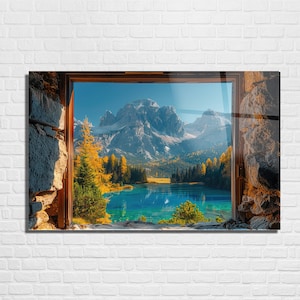 May include: A framed print depicting a mountain lake scene. The image shows a turquoise lake surrounded by autumnal trees, with snow-covered mountains in the background. The frame is dark wood, and the print is mounted on a white brick wall.