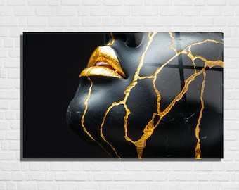 May include: A black sculpture of a face with gold lips and gold-filled cracks. The artwork is displayed on a white brick wall. The face is turned to the side, with the lips prominently featured.
