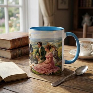 May include: White ceramic mug with a light blue interior and handle. The mug features a pastoral scene with figures in period clothing. A book and a spoon are on a wooden table.