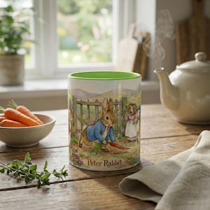 May include: A ceramic mug featuring a Peter Rabbit illustration. The mug has a green interior and a detailed scene of Peter Rabbit in a blue jacket, holding a carrot. The mug is on a wooden table with a teapot and bowl of carrots.