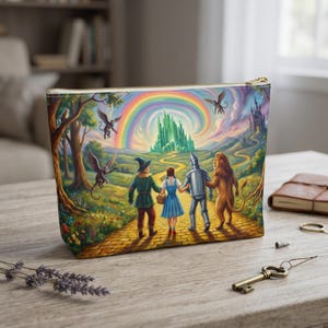 May include: A rectangular zippered pouch featuring a colourful illustration of four figures walking on a yellow brick road towards a green castle under a rainbow. The scene includes flying monkeys, trees, and a distant palace in a vibrant, detailed style.