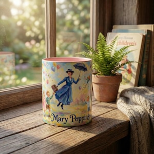 May include: A cylindrical ceramic mug featuring a colorful illustration of Mary Poppins with children and kites. The mug has a pink interior and the words "Mary Poppins" in blue script. The mug is set on a wooden surface near a window.