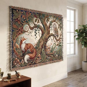 May include: A rectangular woven tapestry blanket featuring a detailed forest scene with a red fox sitting near the base of a large oak tree, an owl perched on a branch, and various mushrooms and acorns in shades of green, brown, and cream.