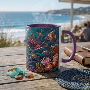 May include: A ceramic coffee mug with a purple handle and interior, depicting a vibrant underwater scene. The design includes an anchor, fish, coral, and a sea turtle. The mug is on a wooden table with sea glass and a coaster.