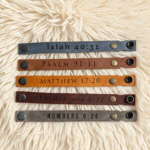 May include: Five leather wristbands in various colors: blue, brown, tan, burgundy, and gray. Each band features a scripture reference: Isaiah 40:31, Psalm 91:11, Matthew 17:20, Philippians 4:13, and Numbers 6:24. Each band has a snap closure.