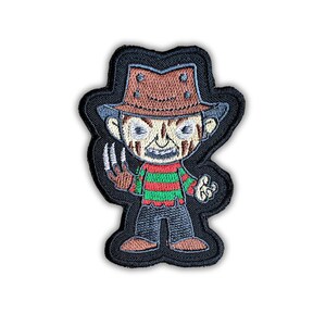 Puede incluir: Parche bordado con una versión de dibujos animados de un personaje de película de terror. El personaje lleva un sombrero marrón, un suéter a rayas rojas y verdes y tiene un guante con garras. El parche tiene un borde negro y está sobre un fondo blanco.