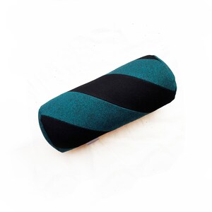Peut inclure: Un coussin cylindrique rayé bleu sarcelle et noir. Le coussin est fait d'un tissu doux et texturé.