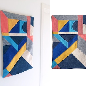 Könnte beinhalten: Ein farbenfroher geometrischer Wandbehang aus Stoffquadraten in Blautönen, Gelb, Rot und Grau. Die Stoffquadrate sind zu einem modernen abstrakten Design zusammengenäht.