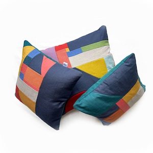 May include: Three decorative throw pillows with patchwork designs. The pillows feature a variety of colors, including navy blue, teal, yellow, orange, red, and purple. The patchwork is made up of geometric shapes.