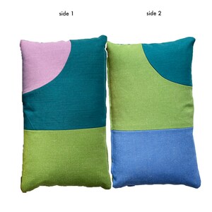 Peut inclure: Deux oreillers rectangulaires avec des motifs g&eacute;om&eacute;triques diff&eacute;rents de chaque c&ocirc;t&eacute;. Un c&ocirc;t&eacute; pr&eacute;sente un fond vert sarcelle avec une forme incurv&eacute;e rose et verte. L'autre c&ocirc;t&eacute; pr&eacute;sente un fond vert avec une forme incurv&eacute;e bleue et verte.