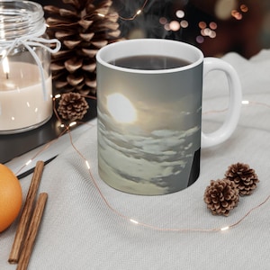 Könnte beinhalten: Weiße Keramik-Tasse mit einem umlaufenden Bild eines bewölkten Himmels und einer hellen Sonne. Die Tasse ist mit einer dunklen Flüssigkeit gefüllt und hat einen weißen Henkel. Die Tasse steht auf einer hellgrauen Oberfläche mit dekorativen Elementen.