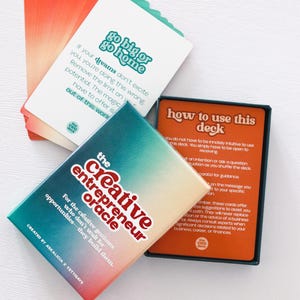 May include: A deck of oracle cards with the text "go big or go home" and "The Creative Entrepreneur Oracle." The cards have a teal, orange, and white color scheme. The deck is designed for creative entrepreneurs.