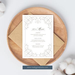 Könnte beinhalten: Eine Menükarte mit ornamentalem floralem Rand, platziert auf einem Holztablett mit einem Kraftpapierumschlag. Die Speisekarte listet Vorspeisen, Hauptgerichte und Dessertoptionen auf. Die Website-Adresse www.reallygreatsite.com befindet sich unten.