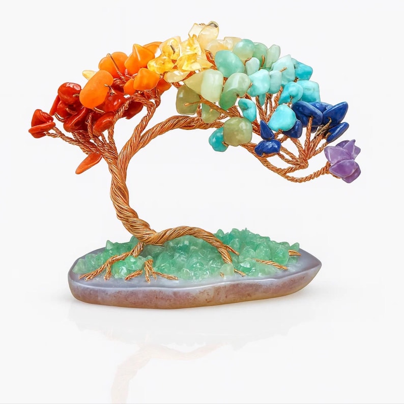 May include: A decorative gemstone tree sculpture. The tree features a copper wire trunk and branches, adorned with colorful gemstones in a rainbow spectrum. The base is a light purple oval with green crystals. A unique and artistic home decor item.