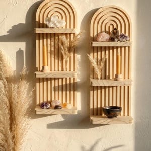 Puede incluir: Dos estanter&iacute;as de pared de madera con una parte superior arqueada y listones verticales. Cada estanter&iacute;a exhibe cristales, velas y plantas secas. Las estanter&iacute;as est&aacute;n montadas en una pared de color claro, creando una est&eacute;tica minimalista y bohemia.