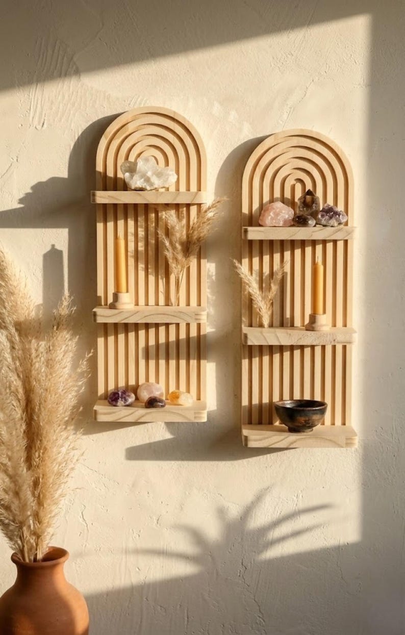Puede incluir: Dos estanter&iacute;as de pared de madera con una parte superior arqueada y listones verticales. Cada estanter&iacute;a exhibe cristales, velas y plantas secas. Las estanter&iacute;as est&aacute;n montadas en una pared de color claro, creando una est&eacute;tica minimalista y bohemia.
