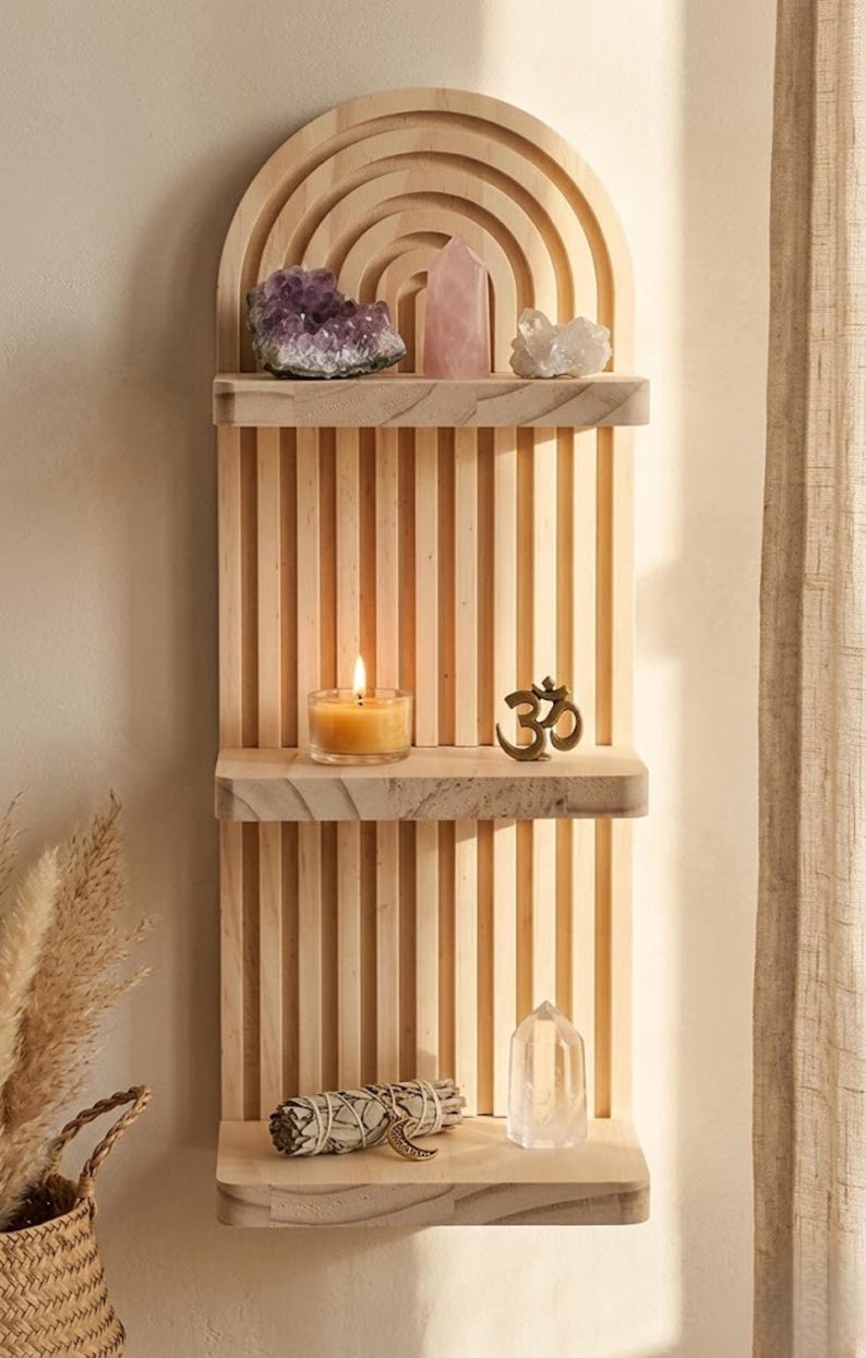 Puede incluir: Estanter&iacute;a de madera en forma de arco&iacute;ris con tres niveles, que muestra cristales, una vela encendida, un s&iacute;mbolo Om de bronce y un manojo de salvia. La estanter&iacute;a es de madera clara y est&aacute; montada en una pared beige.