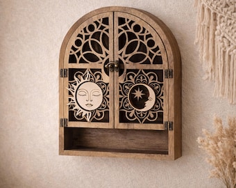May include: Wooden wall-mounted cabinet with an arched top and intricate cut-out designs. The cabinet doors feature a sun and moon design. The cabinet has a small shelf at the bottom and is mounted on a neutral-colored wall.
