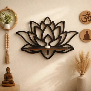 Könnte beinhalten: Schwarzes Lotusblumen-Wandregal mit kleinem Regal und Kerze. Das Regal ist aus Holz und an einer beigefarbenen Wand befestigt. Dekorative Elemente sind eine Buddha-Statue und zwei Korkkreise.