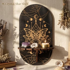 Puede incluir: Estante de altar de cristal de madera negra con un diseño de mariposa y el texto "Crystal Altar Shelf". El estante tiene una pequeña repisa con cristales y una vela encendida. El diseño incluye lunas, estrellas y patrones celestiales.