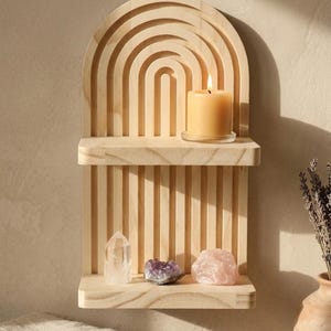Puede incluir: Una estanter&iacute;a de pared de madera con un dise&ntilde;o de arco iris. La estanter&iacute;a contiene una vela encendida, un cristal de cuarzo transparente, amatista y un cuarzo rosa. La estanter&iacute;a es de madera clara y tiene un acabado natural. Un jarr&oacute;n con lavanda est&aacute; a la derecha.