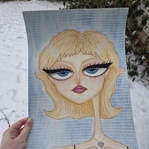 May include: A watercolor portrait of a woman with blonde hair, blue eyes, and a teardrop. The artwork features a thin neck and a heart pendant necklace. The background is a light blue with vertical lines.