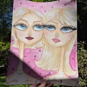 May include: Watercolor painting of two women with blonde hair and large blue eyes. The artwork features a pink background with polka dots. The women are wearing necklaces and the artist's signature is visible.