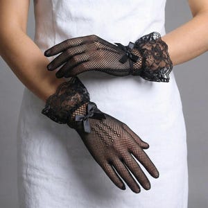 以下が含まれることがあります： 黒いフィッシュネット手袋、レースのカフスと小さな黒いリボン付き。手袋は細かいメッシュ素材で作られており、繊細でフェミニンなデザインです。レースのカフスが全体的な外観にエレガントさを加えています。