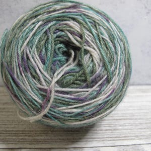 May include: A ball of yarn in shades of green, teal, purple, and white. The yarn is tightly wound, with loose strands visible. This yarn is suitable for knitting and crochet projects.