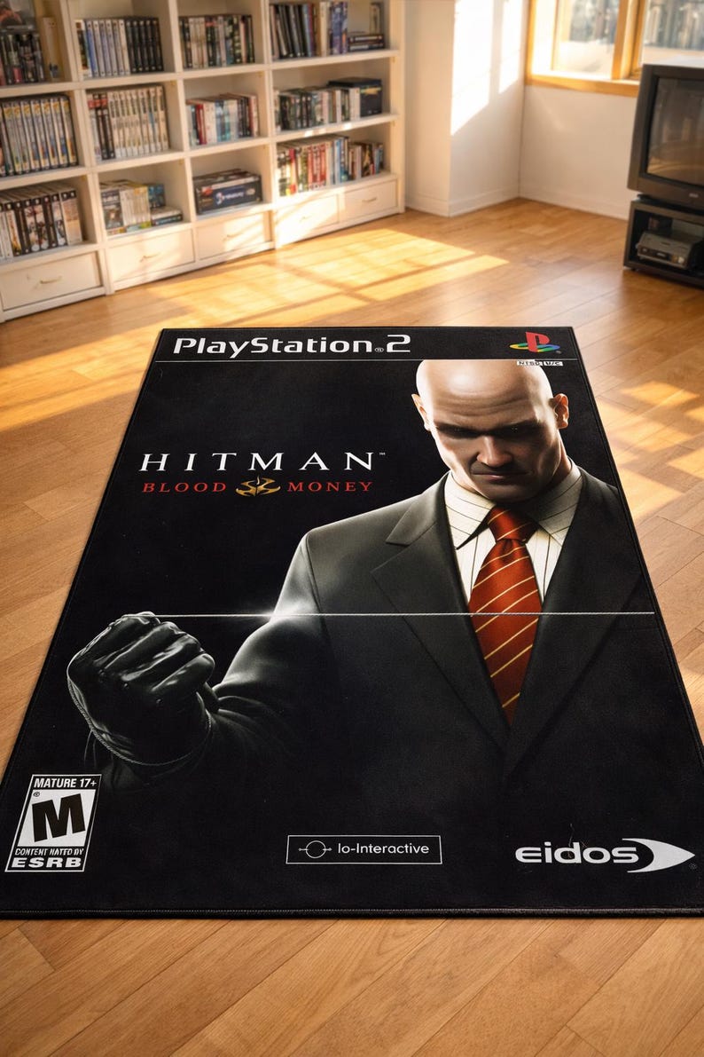 May include: A rectangular area rug featuring the PlayStation 2 video game cover art for Hitman Blood Money. The design displays a bald character in a black suit and red tie, the game title, the ESRB M rating, and the Io-Interactive and Eidos logos.