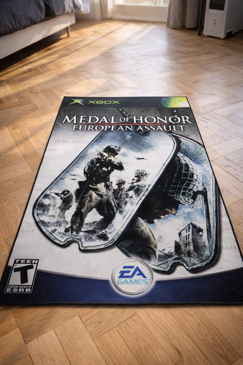 May include: A rectangular area rug featuring the Medal of Honor European Assault video game cover art for Xbox. The design displays soldiers in combat within a dog tag graphic, the EA Games logo, and an ESRB Teen rating symbol on a light background.