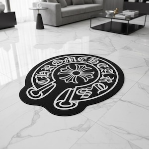 Pode incluir: Tapete decorativo preto e branco com um design de emblema distinto. O tapete apresenta um motivo floral central rodeado por letras estilizadas. O tapete é colocado sobre um chão de mármore branco, adicionando um toque de elegância à divisão.