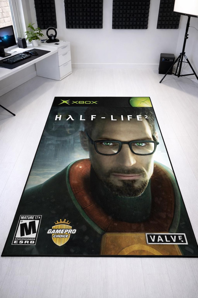 May include: A rectangular area rug featuring the Half-Life 2 video game cover art for Xbox. The design displays a portrait of a man with glasses, the Xbox logo, the Valve logo, a Mature 17+ ESRB rating, and a GamePro Choice gold shield emblem.
