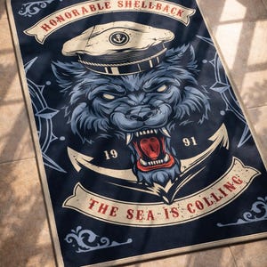 Może przedstawiać: Prostokątny granatowy dywan z warczącym wilkiem w czapce marynarskiej. Dywan zawiera napis "HONORABLE SHELLBACK" i "THE SEA IS CALLING". Grafika wilka jest w odcieniach niebieskiego, z czerwonym pyskiem i białymi zębami.