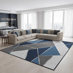 May include: A contemporary geometric rug in a living room setting. The rug's design incorporates blue, grey, and white triangular shapes, outlined with silver lines. The rug is placed in front of a beige corner sofa, with large windows behind.