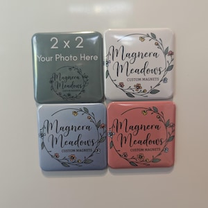 Könnte beinhalten: Vier quadratische Magnete mit abgerundeten Ecken. Einer ist salbeigrün mit dem Text "2 x 2" und "Your Photo Here". Die anderen sind weiß, hellblau und rosa, jeweils mit "Magnera Meadows CUSTOM MAGNETS" in einem Blumenkranz.