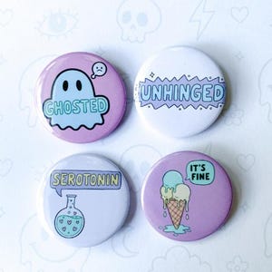 May include: A pack of four pastel-colored button pins. Designs include a ghost with the word "Ghosted", the word "Unhinged", a beaker with the word "Serotonin", and an ice cream cone with the phrase "It's Fine". The text "Pastel Panic" is also visible.