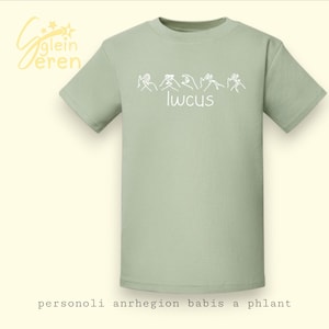 Puede incluir: Una camiseta verde claro con texto blanco y gestos con las manos. La palabra "lwcus" está escrita en blanco debajo de los gestos con las manos. La camiseta también tiene el texto "personoli anrhegion babis a phlant" en la parte inferior.