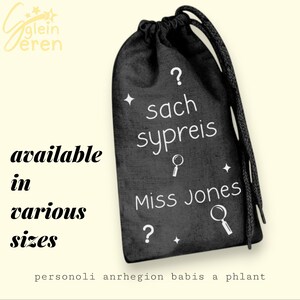 May include: Black drawstring bag with white text and illustrations. The bag features the words "sach sypreis" and "Miss Jones", along with question marks and magnifying glass icons. The text "available in various sizes" is also present.