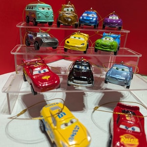 Può includere: Una collezione di modellini di auto giocattolo in vari colori, tra cui rosso, giallo, blu e verde. Le auto sono disposte su un espositore a più livelli, ognuna con un anello per appenderle. Il tema è un giocattolo per bambini o da collezione.