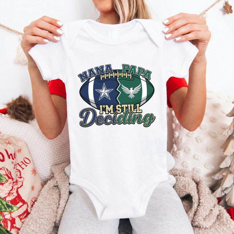 May include: White baby onesie with a football graphic. The graphic includes the words "NANA PAPA" above a split football design with a star and a bird. Below the football is the text "I'M STILL Deciding".