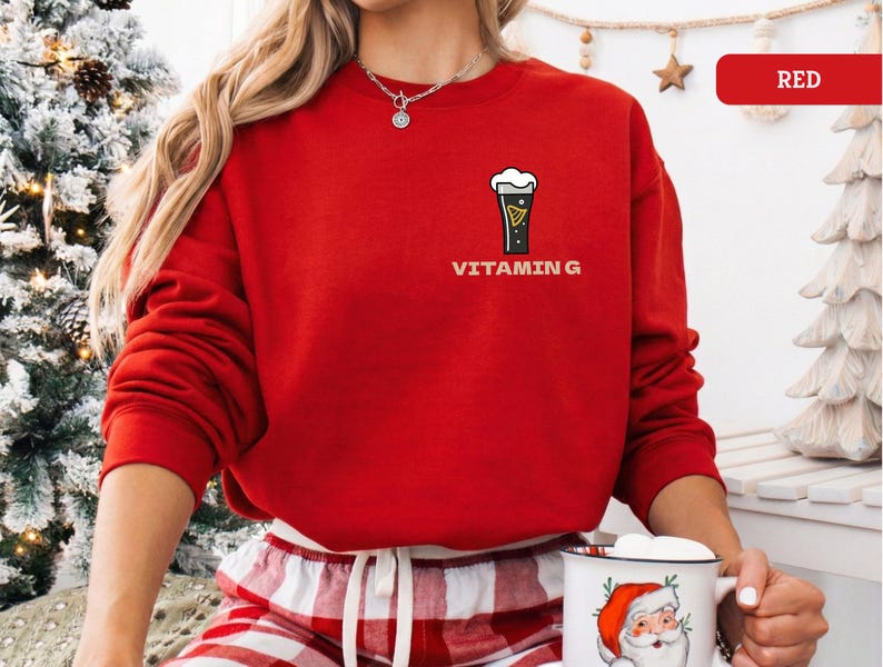 Puede incluir: Una sudadera roja brillante con un gr&aacute;fico de una pinta de cerveza negra y el texto "VITAMIN G". La sudadera de manga larga se usa con pantalones de pijama a cuadros rojos y blancos. Tambi&eacute;n se ve un collar.