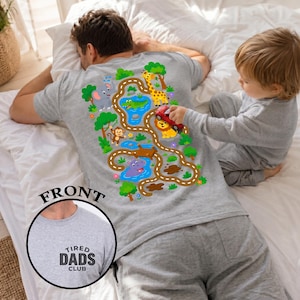 May include: Gray sleep set featuring a playful jungle-themed design on the back of the shirt. The design includes a road with animals like an elephant, giraffe, and lion. The shirt also has the text "TIRED DADS CLUB".