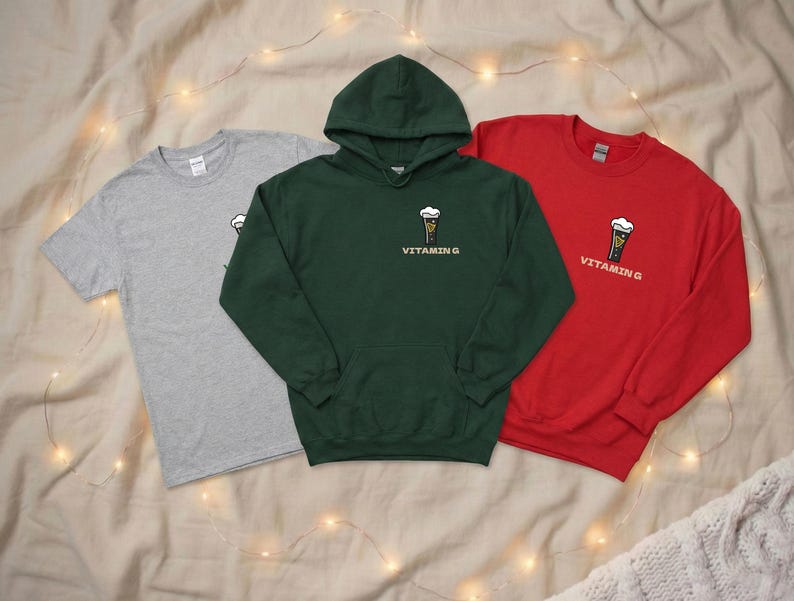 Puede incluir: Tres prendas de vestir: una camiseta gris, una sudadera con capucha verde y una sudadera roja de cuello redondo. Cada art&iacute;culo presenta un peque&ntilde;o gr&aacute;fico de una cerveza con espuma y el texto "VITAMIN G".